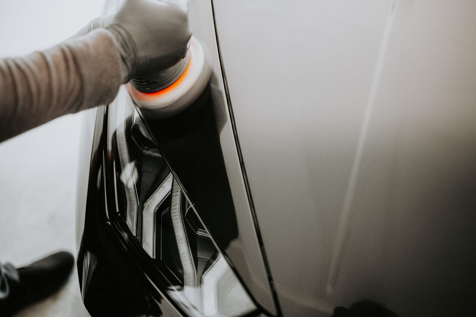 Close-up of ceramic coating applied to a vehicle panel, gloved hands visible, high-gloss reflection showing depth of finish